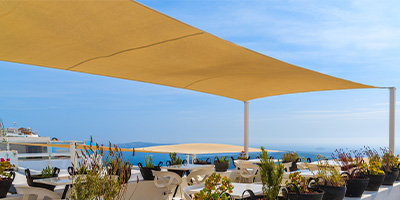 voile rectangulaire ajourée de couleur jaune moutarde sur une terrasse de restaurant